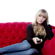 young blond haired girl on red sofa with remote control