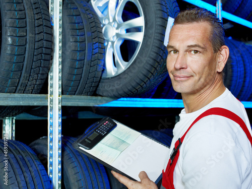 Photo: Mechanic looking for the right tires with car registration book Mechanic looking for the right tires with car registration book