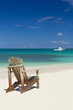 Beach chair on sandy beach with white boat on background