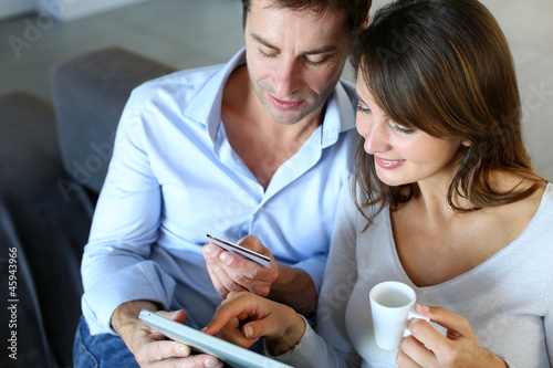 Photo: Mature couple at home using credit card to shop online Mature couple at home using credit card to shop online
