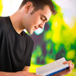 Young happy man reading book or textbook, outdoor