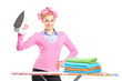 A smiling woman with hair rollers holding an iron and ironing bo