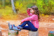 Kid girl sitting in forest trunk looking far away