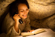 Smiling Woman Reading a Book with Flashlight on Bed