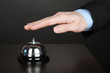 Hand ringing in service bell on wooden table on black