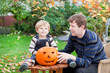 Young man and toddler boy making halloween pumpkin