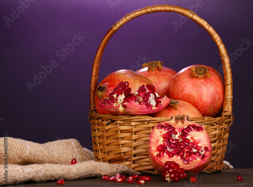 Photo: Ripe pomegranates on basket on wooden table on purple Ripe pomegranates on basket on wooden table on purple
