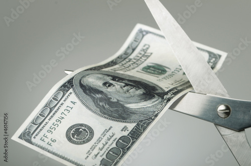Photo: Scissors cutting a dollar bill in half Scissors cutting a dollar bill in half