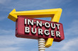 A classic IN-N-OUT BURGER sign in front of sky with yellow arrow