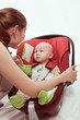 The young woman fastens the child in an armchair for the car