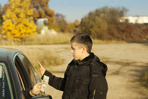 Photo: Someone from the car is offering money to the boy Someone from the car is offering money to the boy
