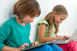 Two kids playing on tablet and laptop.