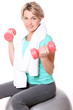 Cute mid aged women with towel do exercises with dumbbells