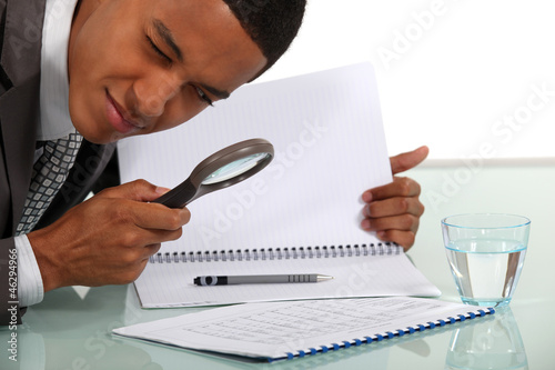 Photo: Man examining a document with a magnifying glass Man examining a document with a magnifying glass