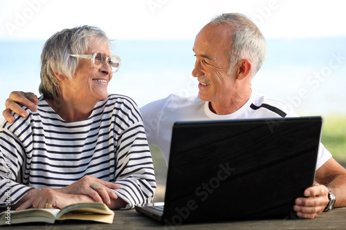 Photo: Senior couple in the garden with laptop and book Senior couple in the garden with laptop and book