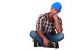 A pensive construction worker sitting on the floor.