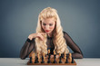 Photo: Beautiful blonde woman playing chess on dark background. Beautiful blonde woman playing chess on dark background.