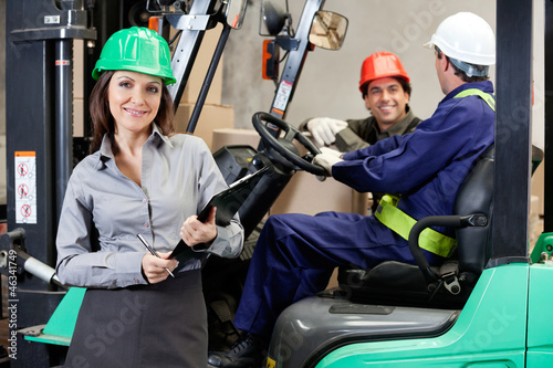 Photo: Confident Female Supervisor With Forklift Driver At Warehouse Confident Female Supervisor With Forklift Driver At Warehouse