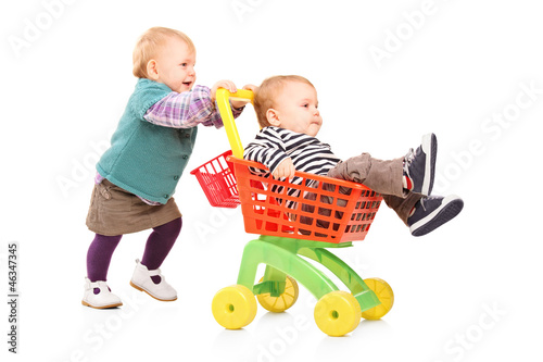Photo: Toddler girl pushing her twin brother in a toy cart Toddler girl pushing her twin brother in a toy cart