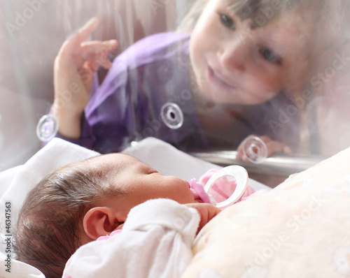Photo: Newborn baby girl in a incubator. Her sister looking at. Newborn baby girl in a incubator. Her sister looking at.