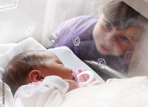 Photo: Newborn baby girl in a incubator. Her sister looking at. Newborn baby girl in a incubator. Her sister looking at.