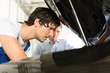 Kunde und Mechaniker an Auto schauen unter Haube