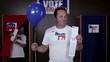 Video: Caucasian man standing in front of voting booth holding balloon and ballot, woman voter exits voting booth popping balloon Caucasian man standing in front of voting booth holding balloon and ballot, woman voter exits voting booth popping balloon