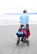 Father pulling disabled son on wheelchair through beach sand