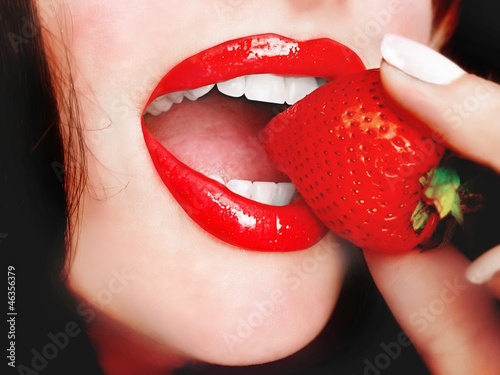 Foto: Sexy young pretty woman with red lips eating a red strawberry Sexy young pretty woman with red lips eating a red strawberry