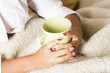 Female hands over blanket with cup of tea