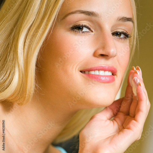 Photo: Happy smiling woman applying creme, indoor Happy smiling woman applying creme, indoor
