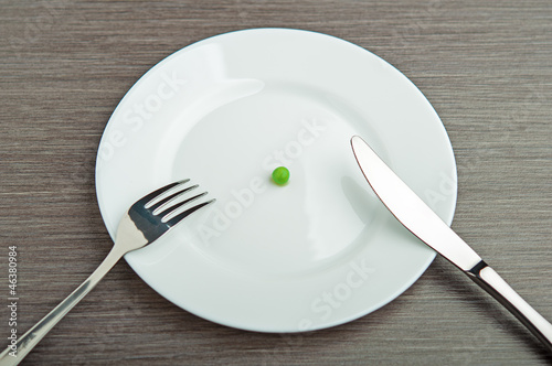 Photo: diet concept. one pea on an empty white plate diet concept. one pea on an empty white plate