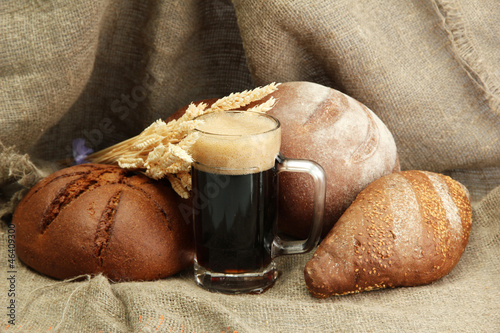 Photo: tankard of kvass and rye breads with ears, on burlap background tankard of kvass and rye breads with ears, on burlap background