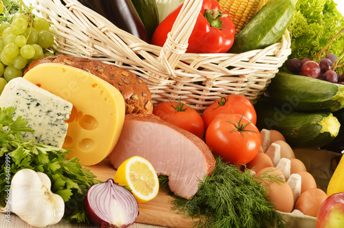 Photo: Composition with groceries in wicker basket on kitchen table Composition with groceries in wicker basket on kitchen table