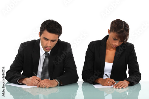 Photo: Two business people writing at a desk Two business people writing at a desk