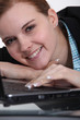 young woman leaning her head on a laptop and smiling