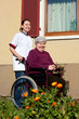 Pflegerin schiebt Seniorin im Rollstuhl