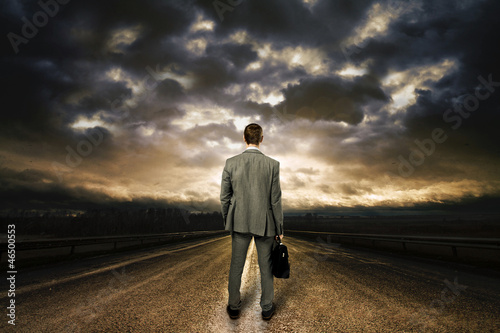 Photo: Business man standing in the middle of the road. Dramatic sky ab Business man standing in the middle of the road. Dramatic sky ab