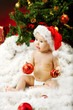 Christmas baby in hat sitting on fur holding red ball