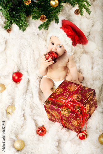 Photo: Christmas baby sitting on fur and eating gift Christmas baby sitting on fur and eating gift