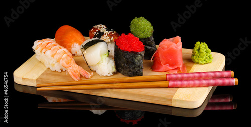 Photo: delicious sushi served on wooden board isolated on black delicious sushi served on wooden board isolated on black