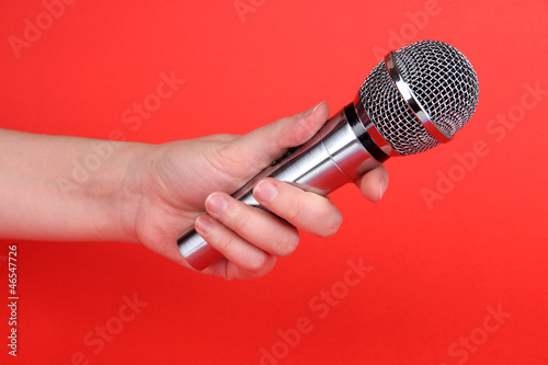 Photo: Silver microphone in hand on red background Silver microphone in hand on red background