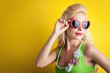 Blonde girl with heart glasses against yellow background.