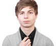 A young man in a gray cardigan straightens his tie