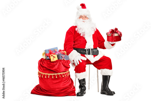 Photo: Santa Claus with a gift sitting next to a bag full of presents Santa Claus with a gift sitting next to a bag full of presents
