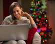 Happy woman looking in laptop in front of Christmas tree