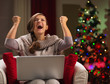 Woman with laptop rejoicing success in front of Christmas tree