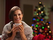 Smiling young woman with cup of chocolate near Christmas tree