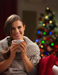 Happy young woman with cup of hot chocolate near Christmas tree