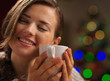 Young woman enjoying cup of beverage near Christmas tree
